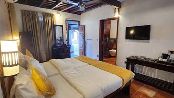 Habitación de hotel con cama, escritorio con cafetera, televisor y zona de ducha.