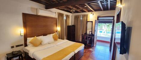 Una habitación de hotel con una cama grande, lámparas de noche, un aire acondicionado, un escritorio con silla y un televisor.
