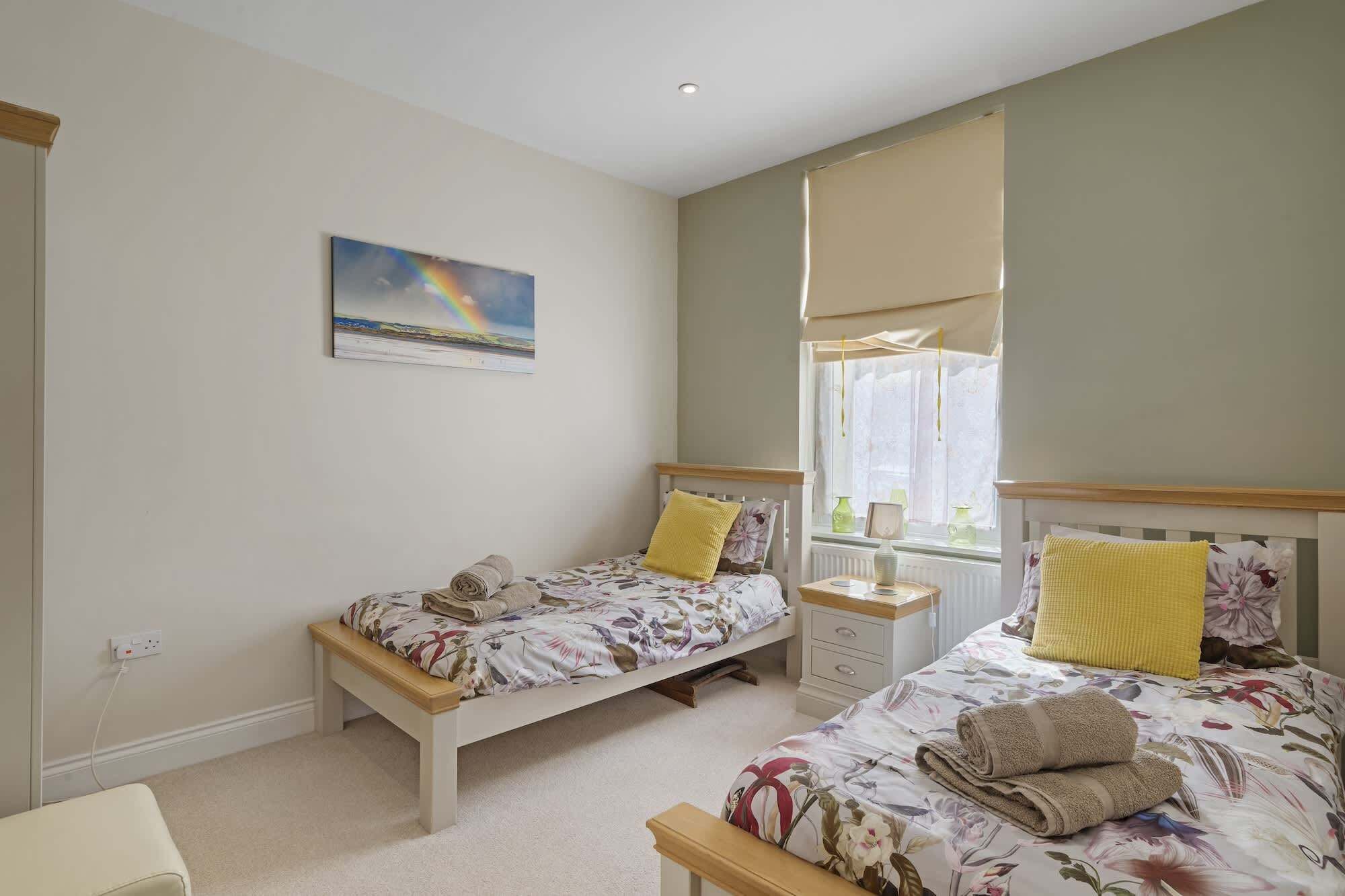 A bedroom with two single beds, a nightstand, a window with curtains, and a painting on the wall.