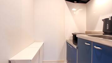 A compact kitchen with white walls, a small window, and blue cabinets.