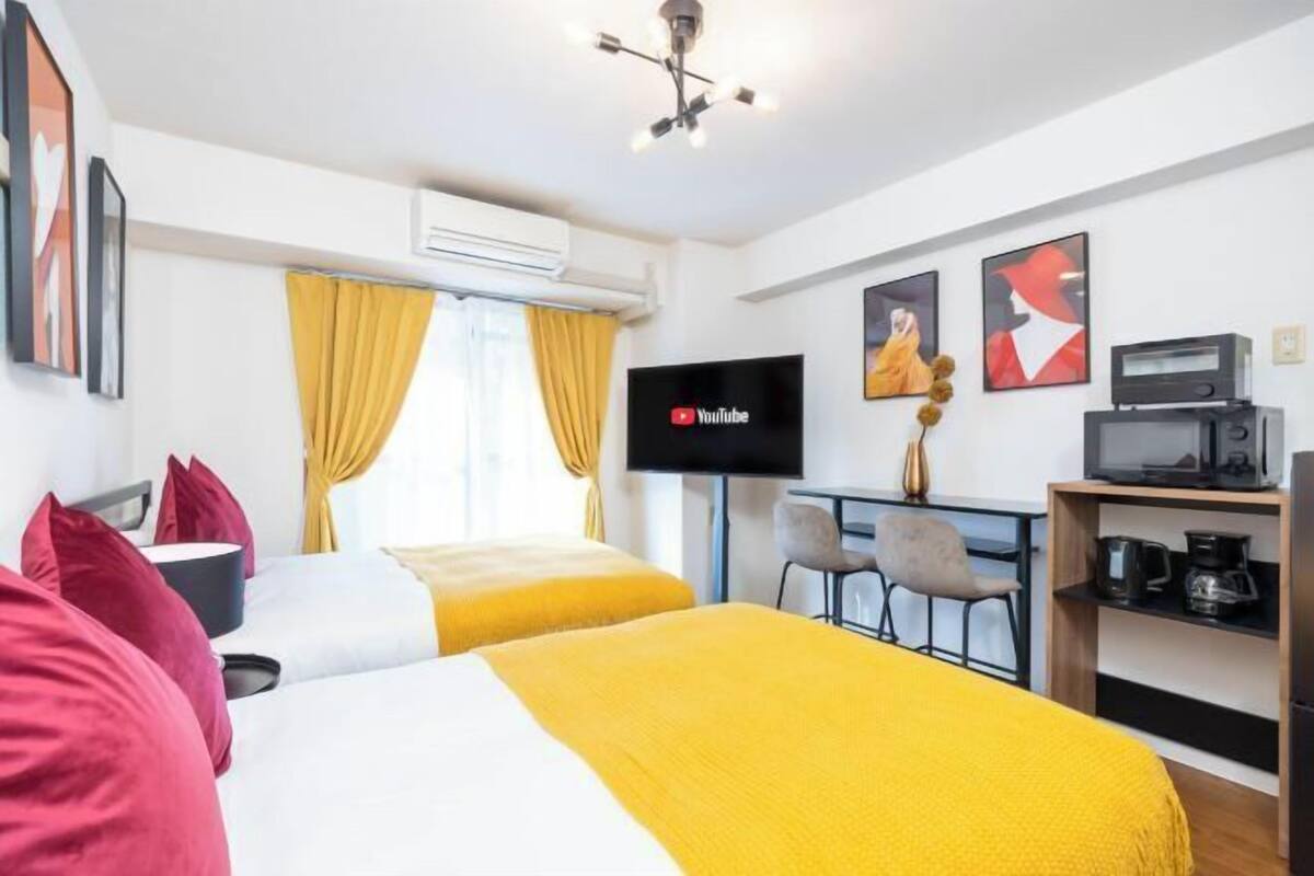 A hotel room with two beds, a TV, a desk with a chair, and a coffee machine.
