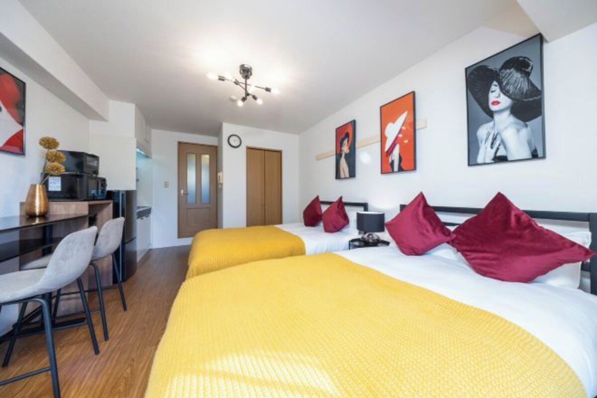 A hotel room with two beds, a desk with chairs, artwork on the walls, and a ceiling light fixture.