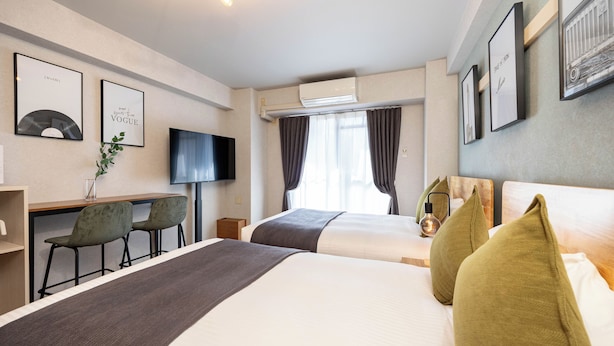 Une chambre d’hôtel avec deux lits, un bureau avec des chaises, une télévision et des tableaux encadrés aux murs.