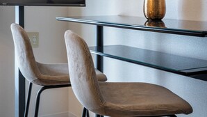 Un espace repas moderne avec une table en verre, deux chaises rembourrées et un vase contenant des fleurs séchées.