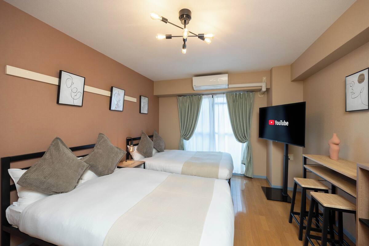 A hotel room with two beds, a TV, and a desk with stools.
