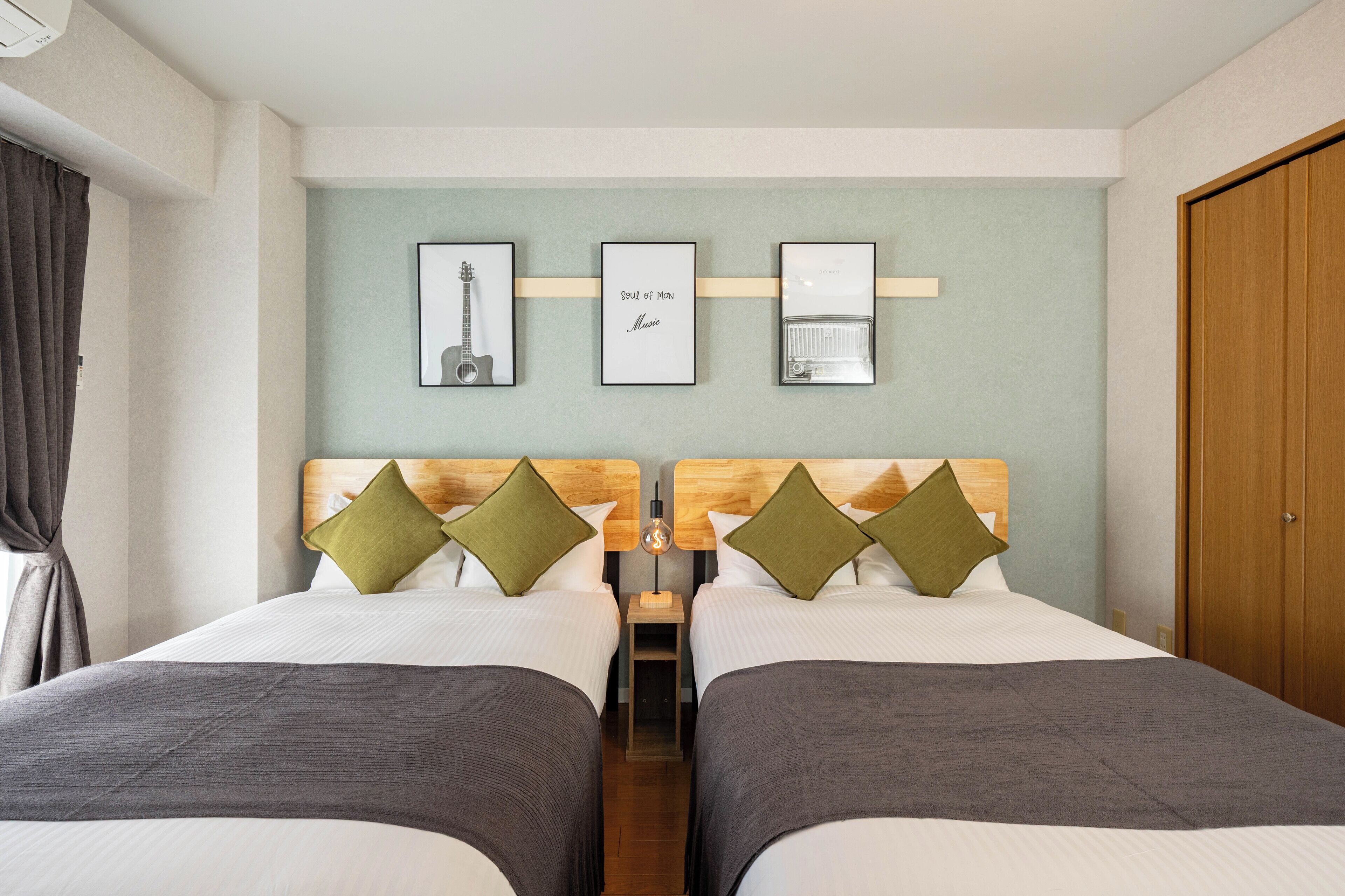 A hotel room with two beds, a wooden headboard, a small table, and framed pictures on the wall.