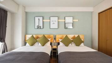 A hotel room with two beds, a wooden headboard, a small table, and framed pictures on the wall.