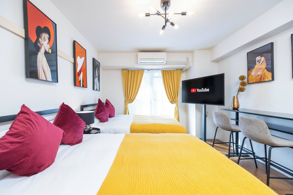 A hotel room with two beds, a TV, a desk with chairs, and artwork on the walls.