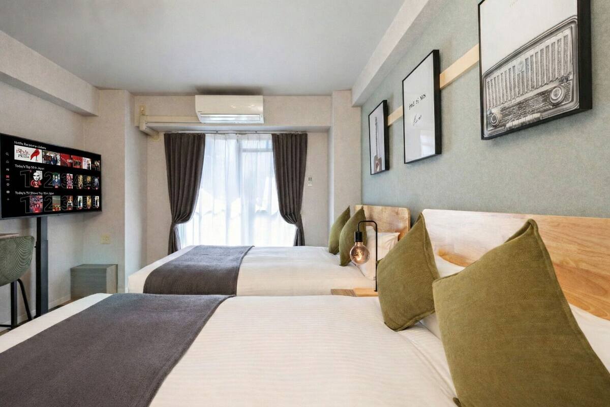 A hotel room with two beds, a TV on the wall, and a window with curtains.