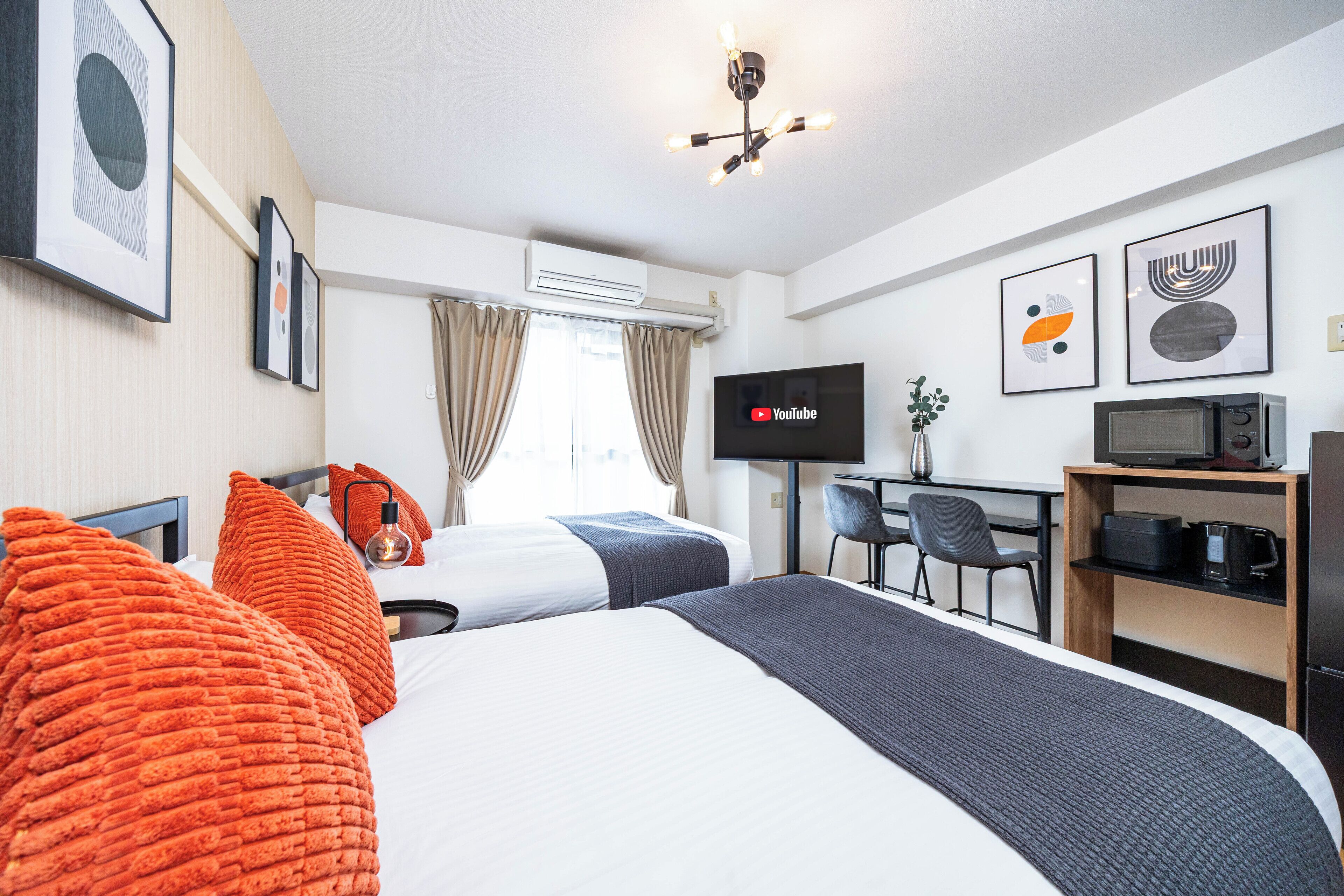 A hotel room with two beds, a desk with a chair, a TV, and a microwave.