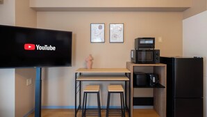 Une cuisine compacte équipée d’une télévision, d’un four à micro-ondes et d’un réfrigérateur. Elle comprend deux tabourets et une petite table.
