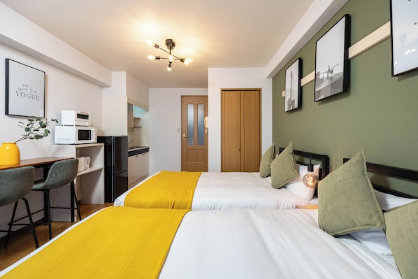 A hotel room with two beds, a desk with a chair, a microwave, and a door leading to a bathroom.