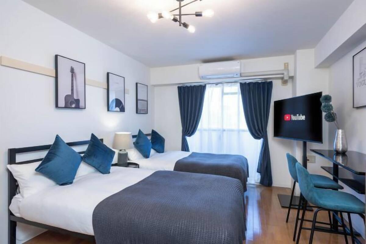 A hotel room with two beds, a TV, a desk, and a window with curtains.