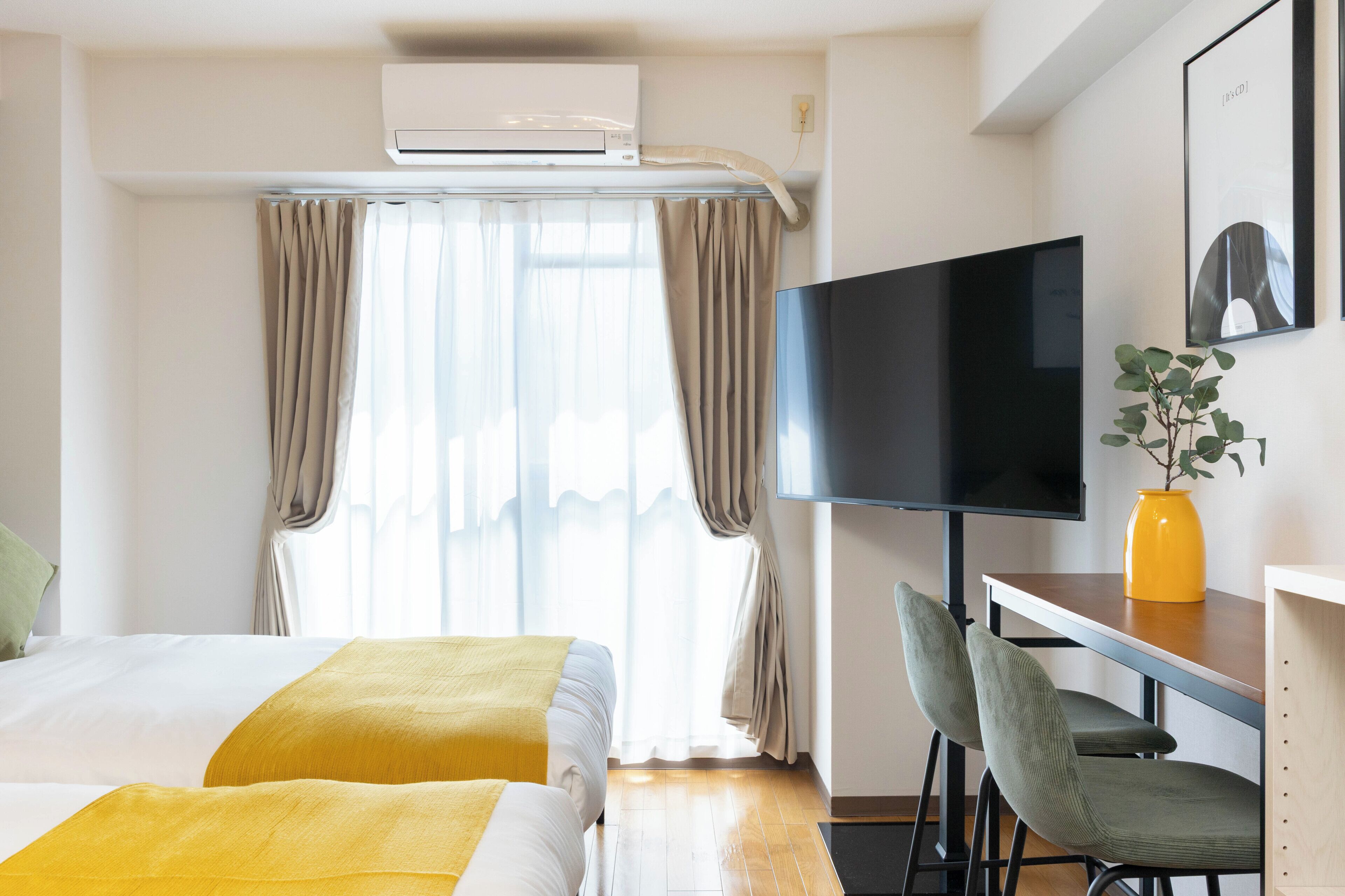 A hotel room with a bed, a desk with a chair, a television, and an air conditioning unit.