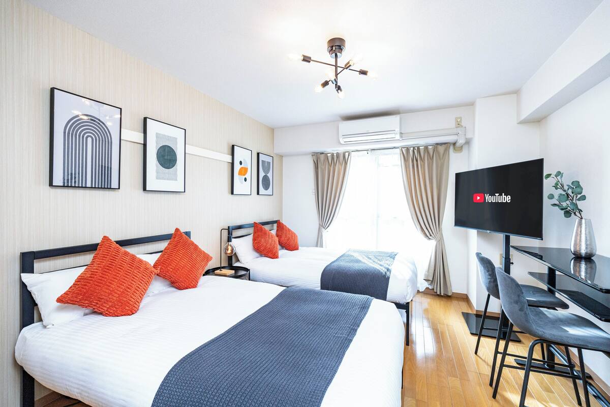 A hotel room with two beds, a TV, a desk with chairs, and framed artwork on the wall.