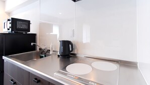 Une cuisine moderne dotée d’un évier en acier inoxydable, d’une bouilloire noire et d’une plaque de cuisson à induction intégrée.