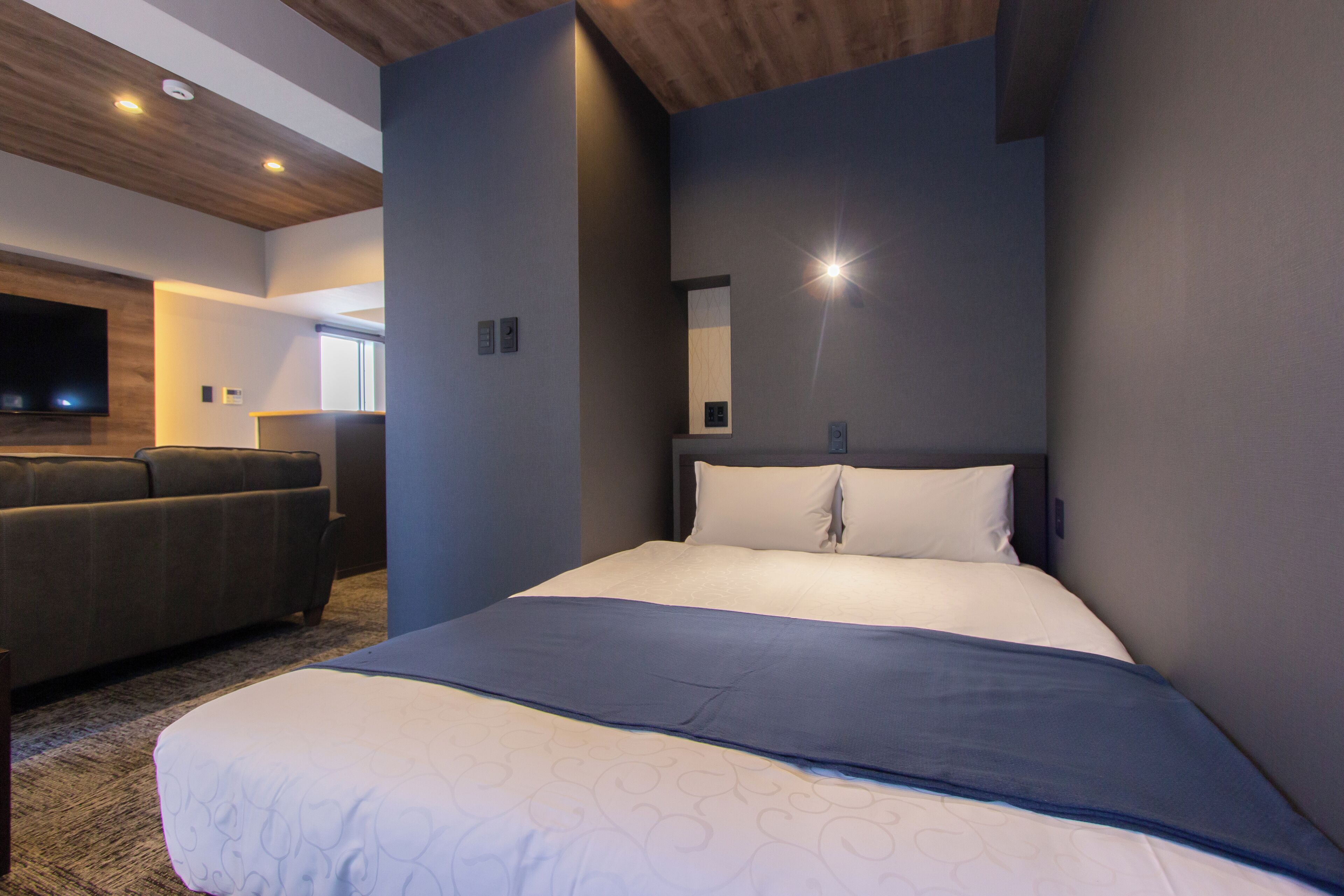 A modern hotel room with a large bed, a flat-screen TV mounted on the wall, and a seating area with a sofa.