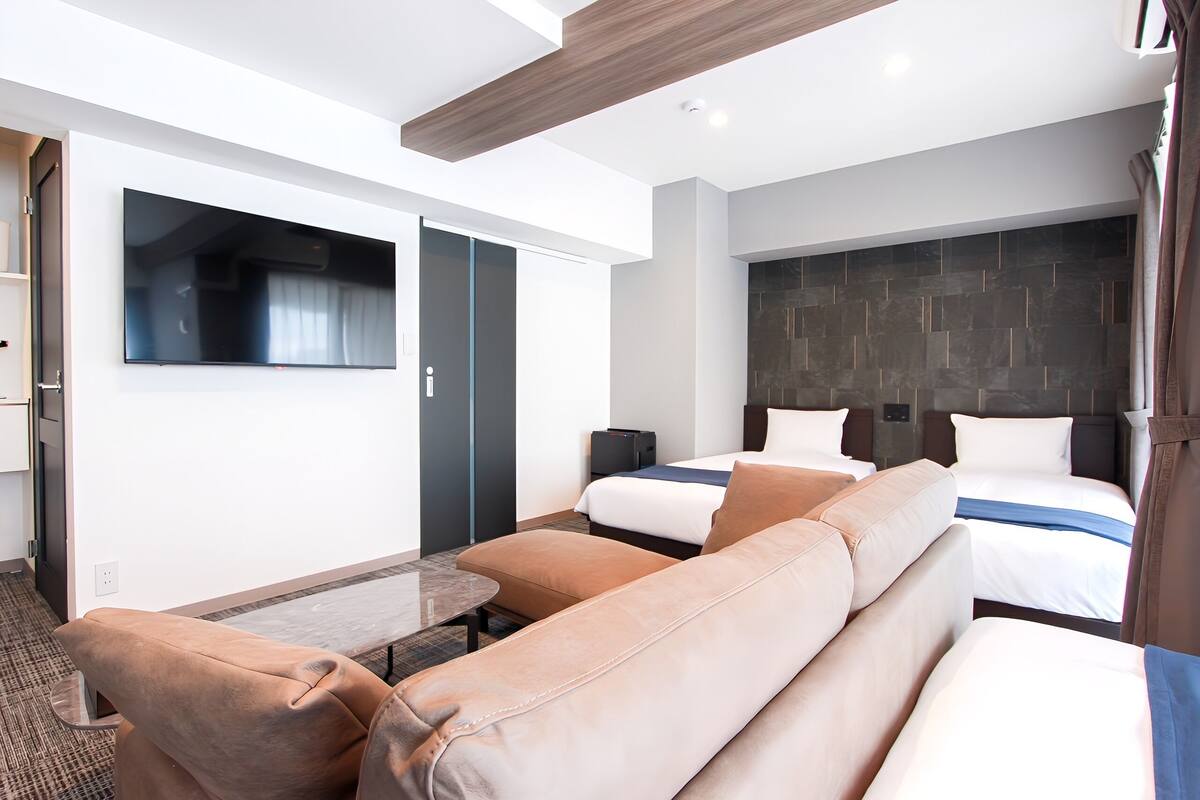 A modern hotel room with a large bed, a sofa, a TV, and a wardrobe.