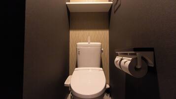 A small, compact bathroom with a toilet, a toilet paper holder, and a wall-mounted shelf.