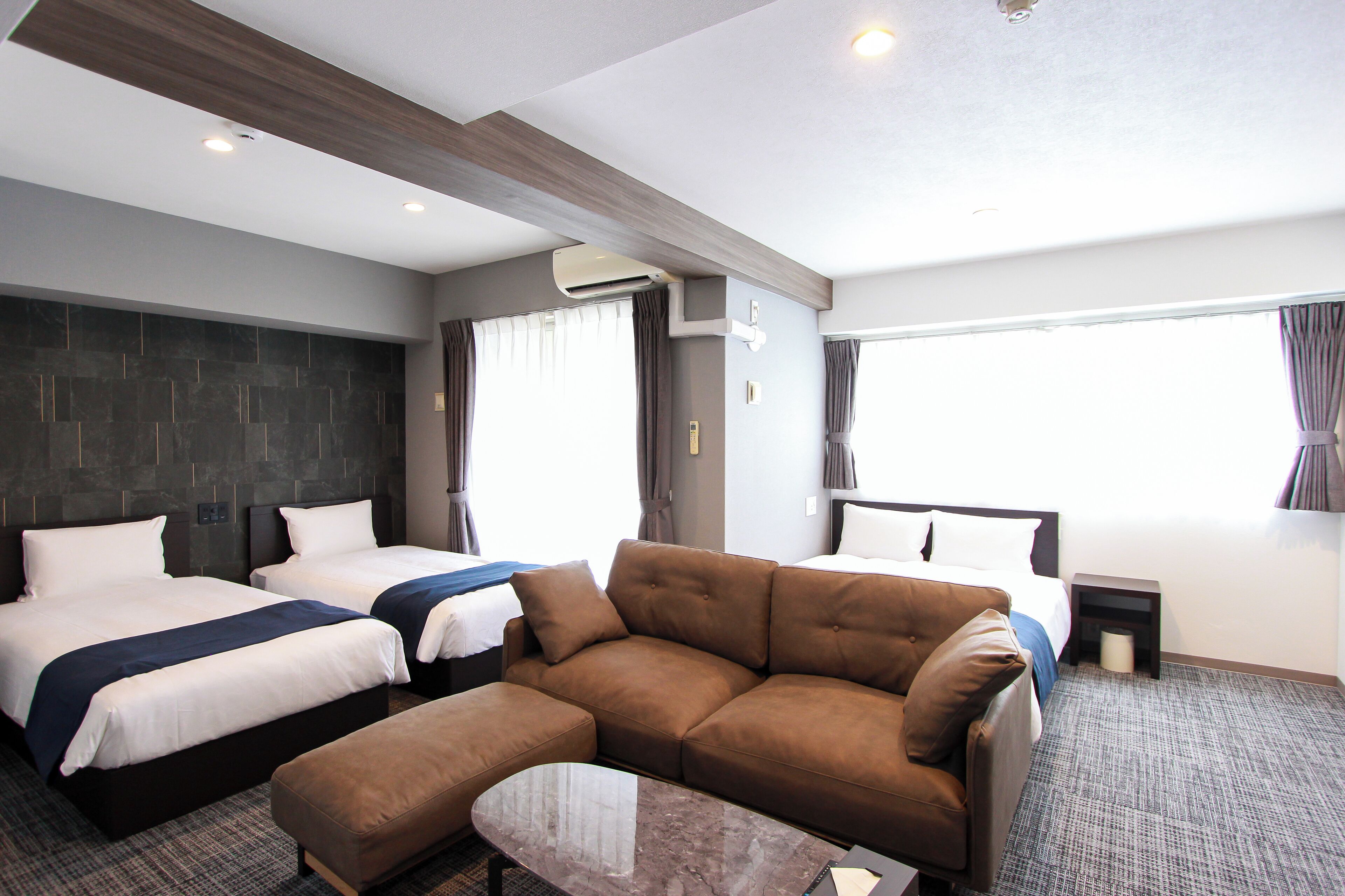 A hotel room with two beds, a sofa, a small table, and a window with curtains.