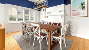A dining area with a wooden table and white chairs, a ceiling light fixture, and a painting on the wall. - Luxury Villas Shelley St (Pet Friendly) (Elwood)