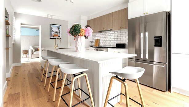 A modern kitchen with a central island, bar stools, a stainless steel refrigerator, and wooden cabinets. - Luxury Villas Shelley St (Pet Friendly) (Elwood)