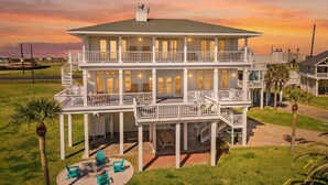 A two-story beachfront house with a balcony, outdoor seating, and a view of the ocean.