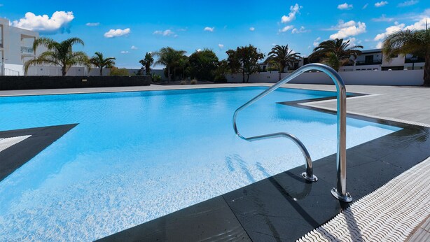 Une piscine à l’eau d’un bleu cristallin, entourée d’une terrasse carrelée et de palmiers.