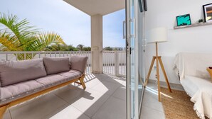 Un balcon avec un canapé, une lampe sur pied et une vue sur des palmiers.