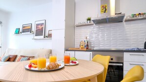 Une cuisine moderne avec des meubles blancs, un four encastré et un coin repas avec des chaises jaunes.