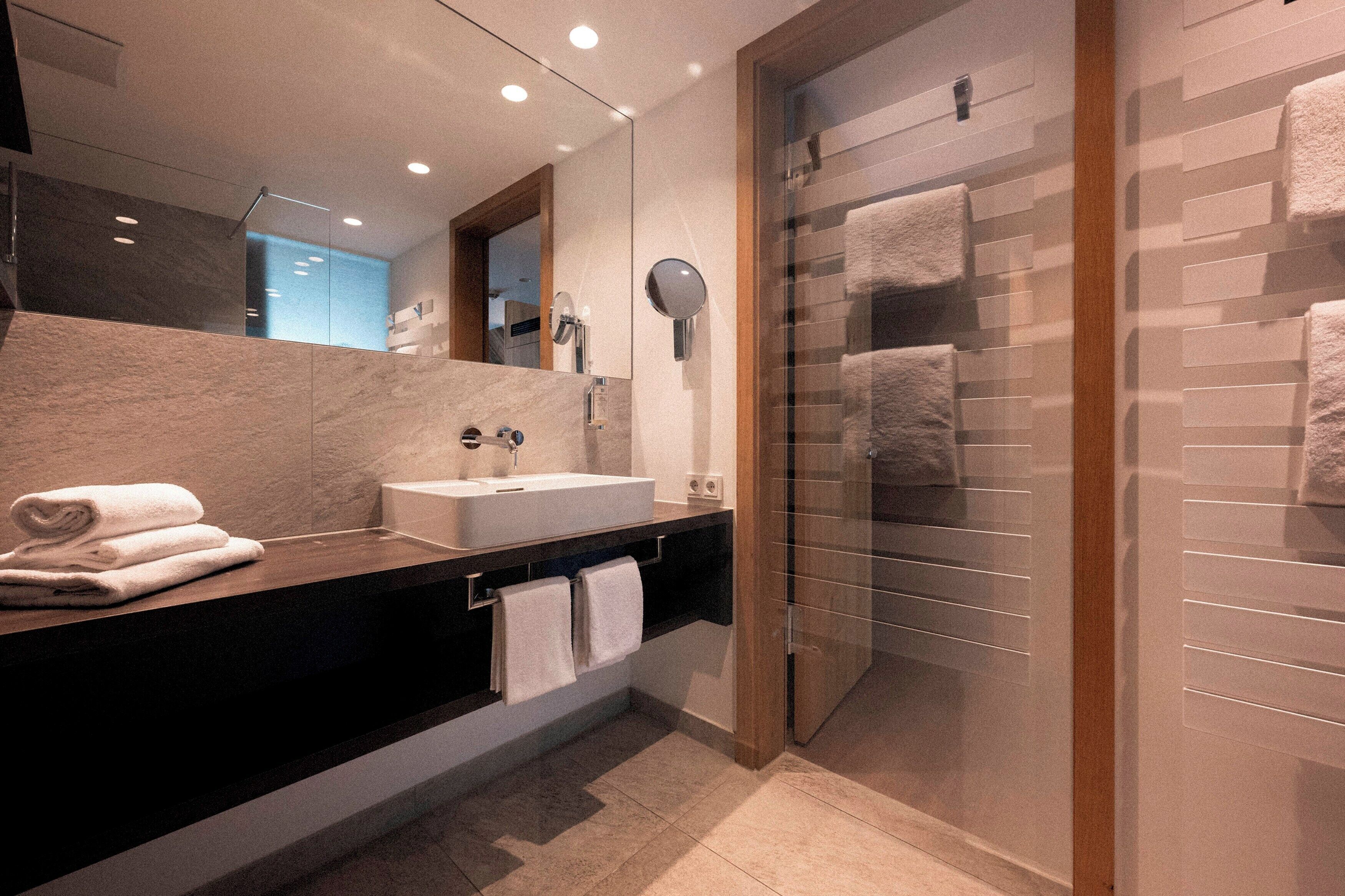 A modern bathroom with a large mirror, a sink, and a glass shower enclosure.