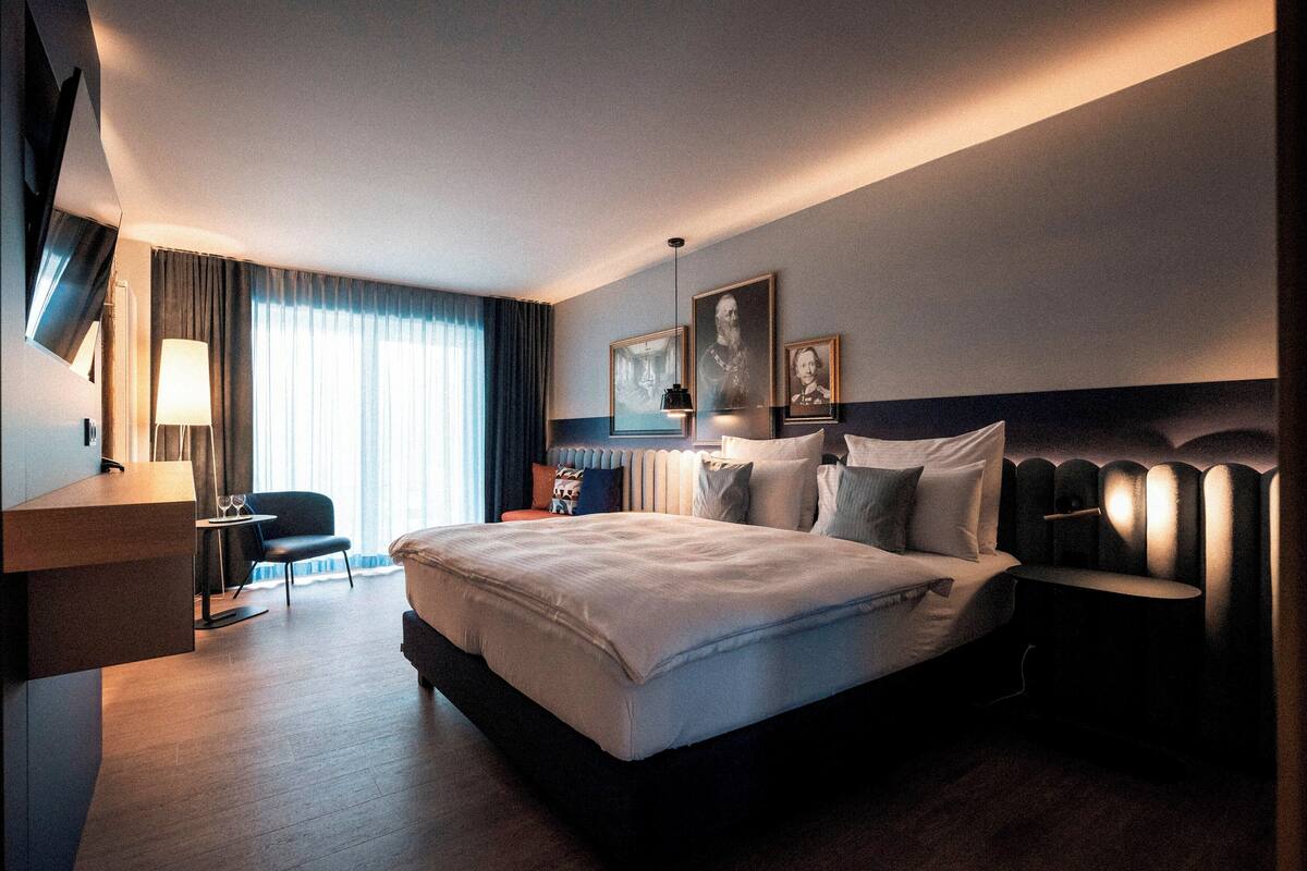 A modern hotel room with a large bed, bedside tables, a desk, and a chair.