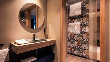 Ein modernes Badezimmer mit einem Holzbadezimmerhocker, einem runden Spiegel und einer Duschkabine mit floralem Wandpapier.