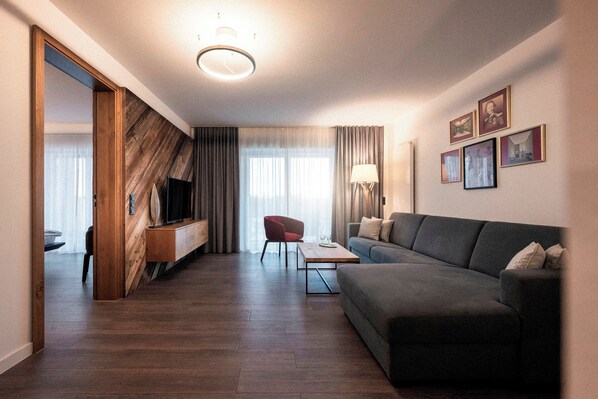 Una sala de estar moderna con un sofá oscuro, un sillón rojo, un mueble de televisión de madera y un televisor de pantalla plana.