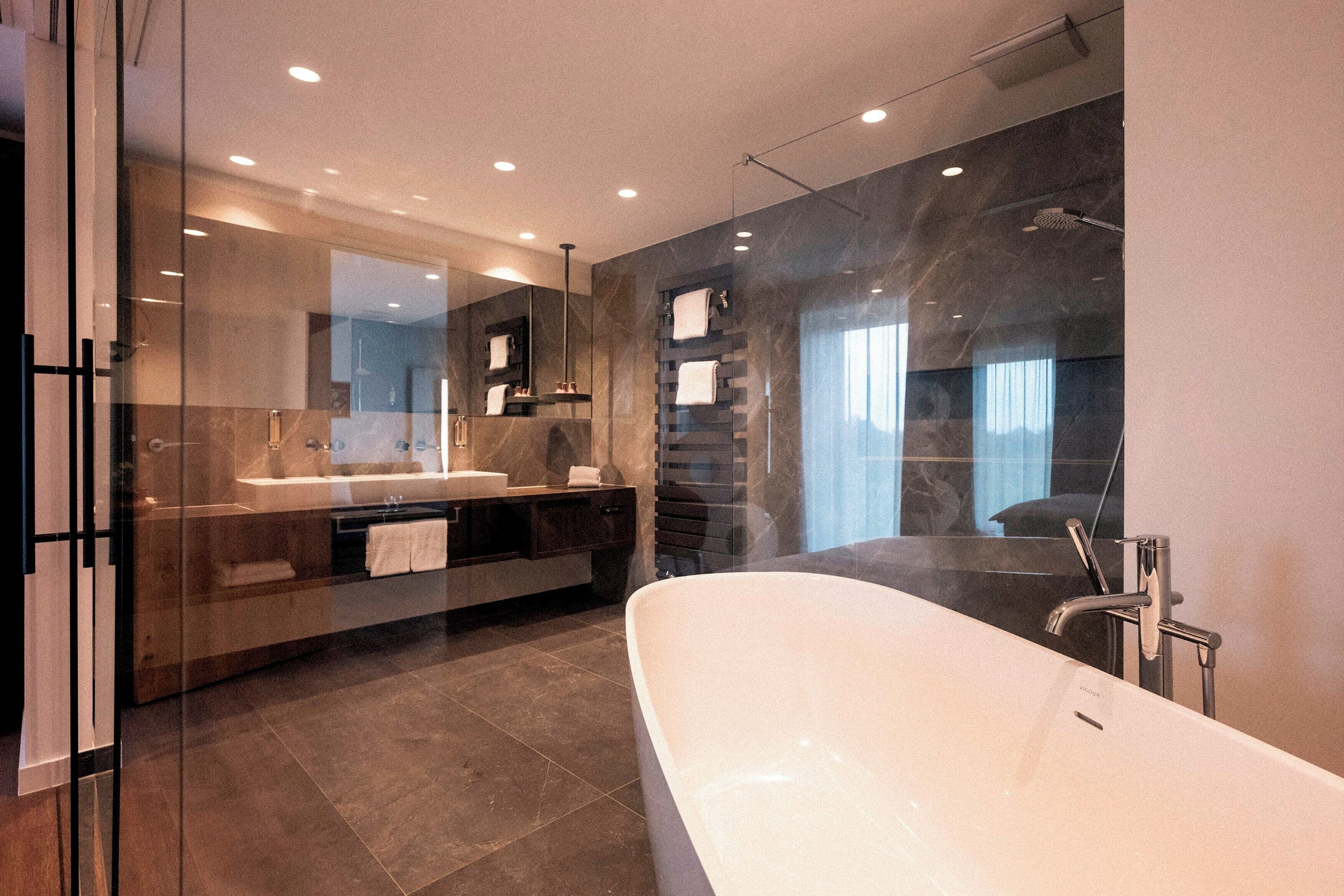 Une salle de bain moderne dotée d’une baignoire sur pieds, d’une douche à parois de verre et d’un meuble-lavabo avec un grand miroir.