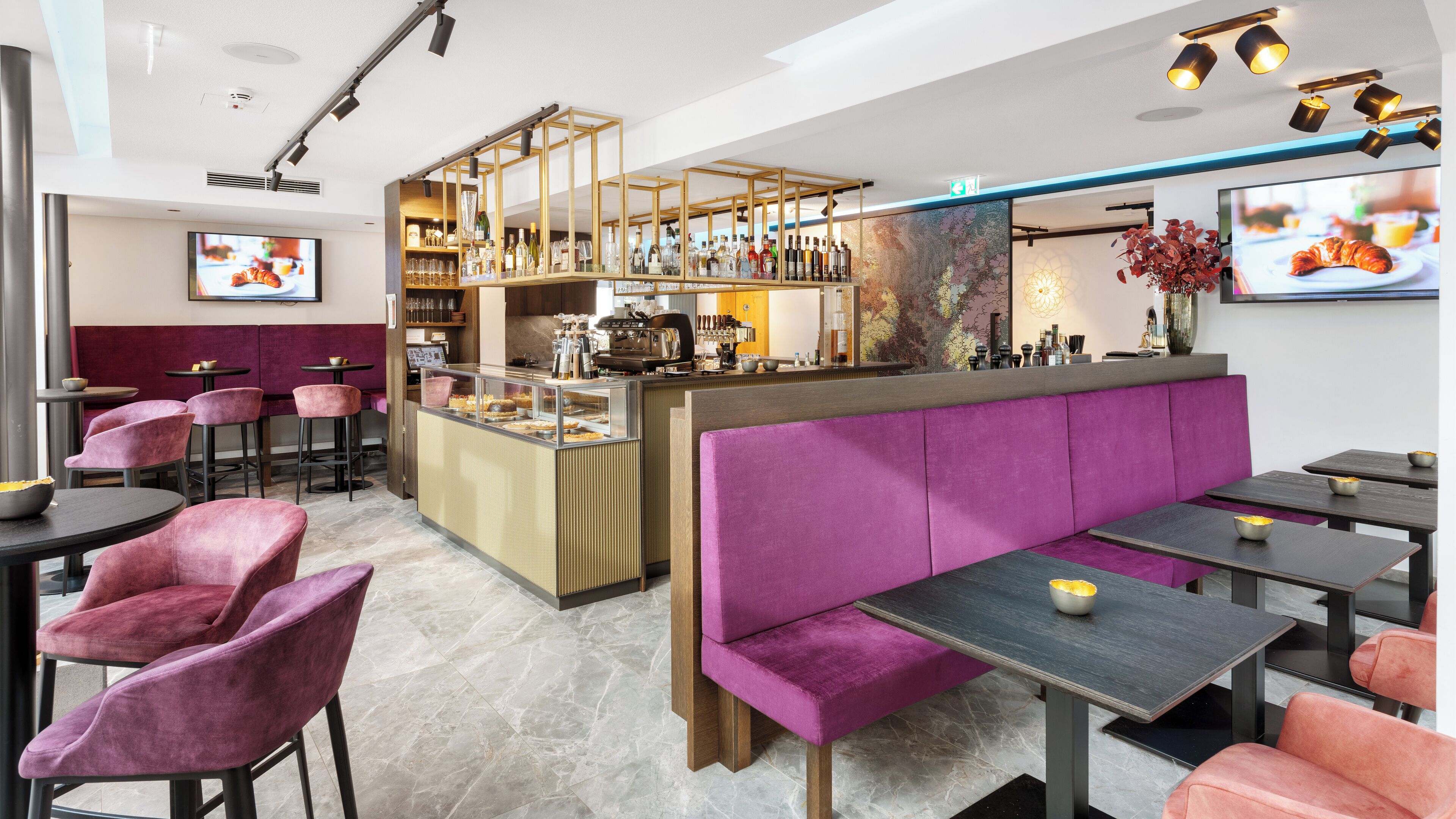 Um café moderno com área de bar, assentos com almofadas roxas e diversas bebidas expostas.