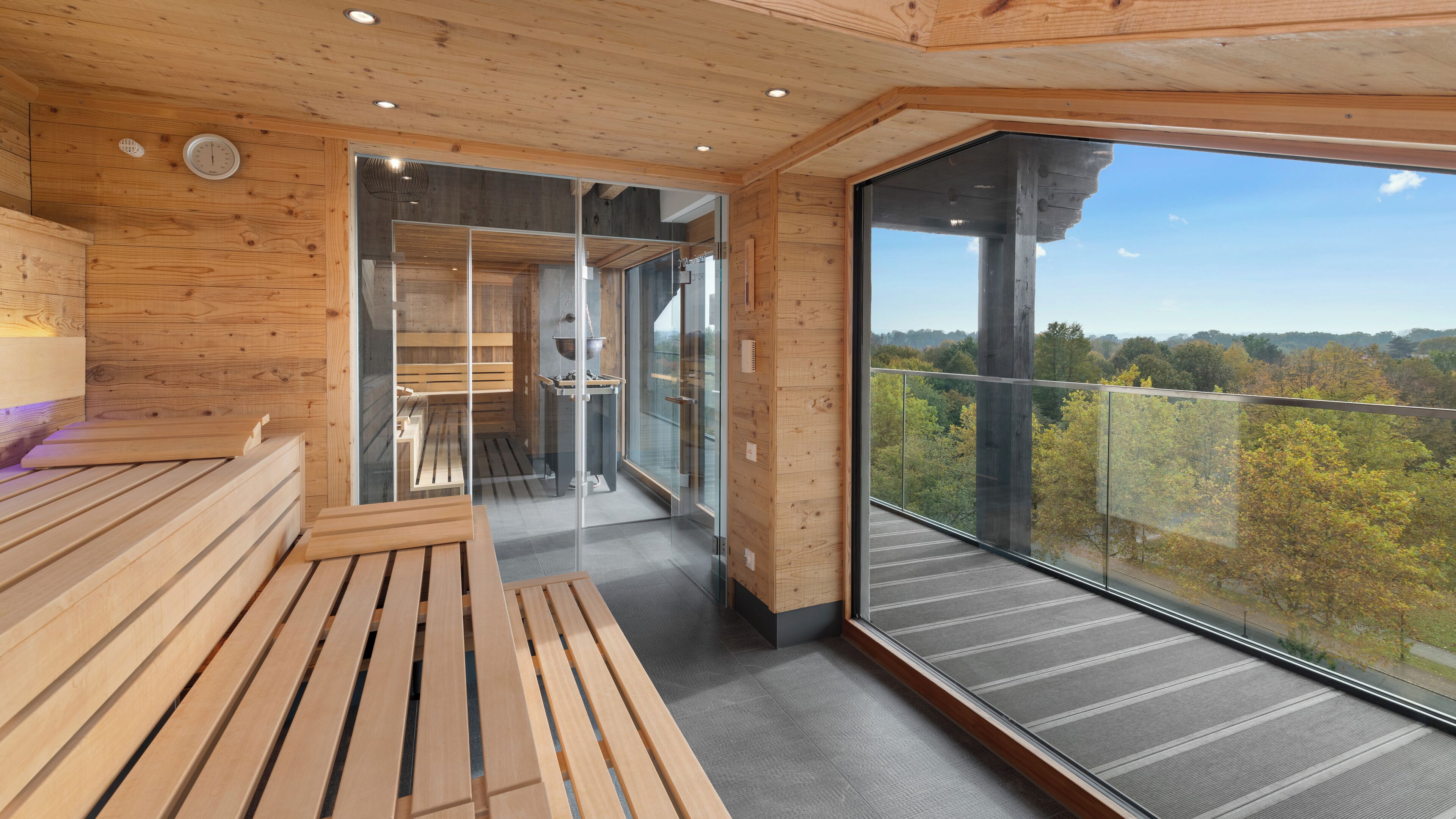 Un interior moderno de madera con un amplio balcón de vidrio con vistas a un área boscosa.
