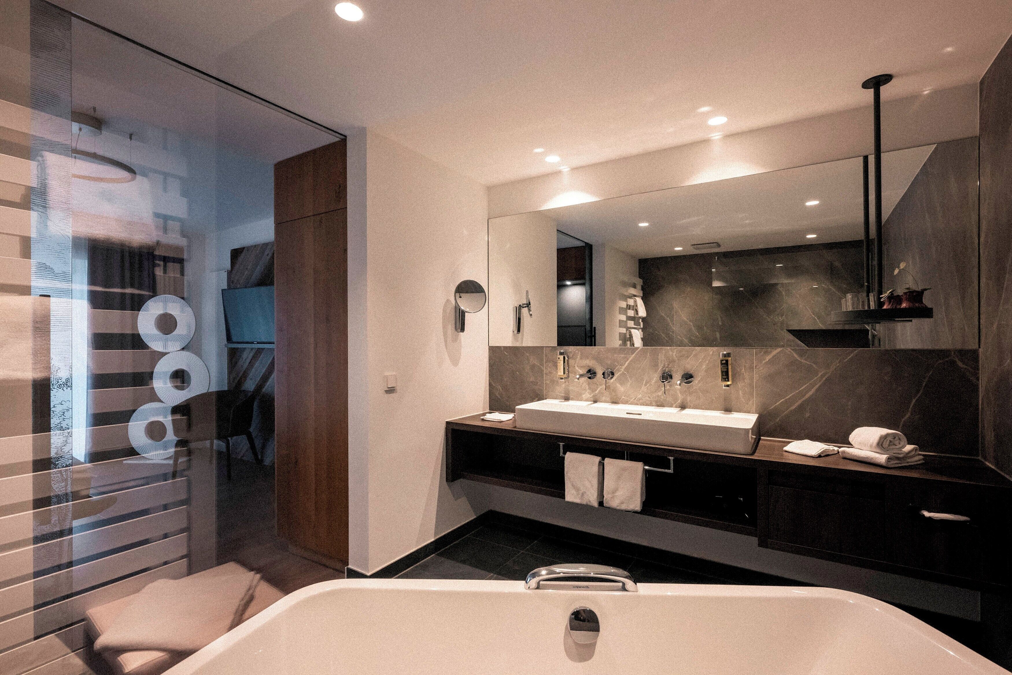 A modern bathroom with a large bathtub, a vanity with a mirror, and a dark marble backsplash.