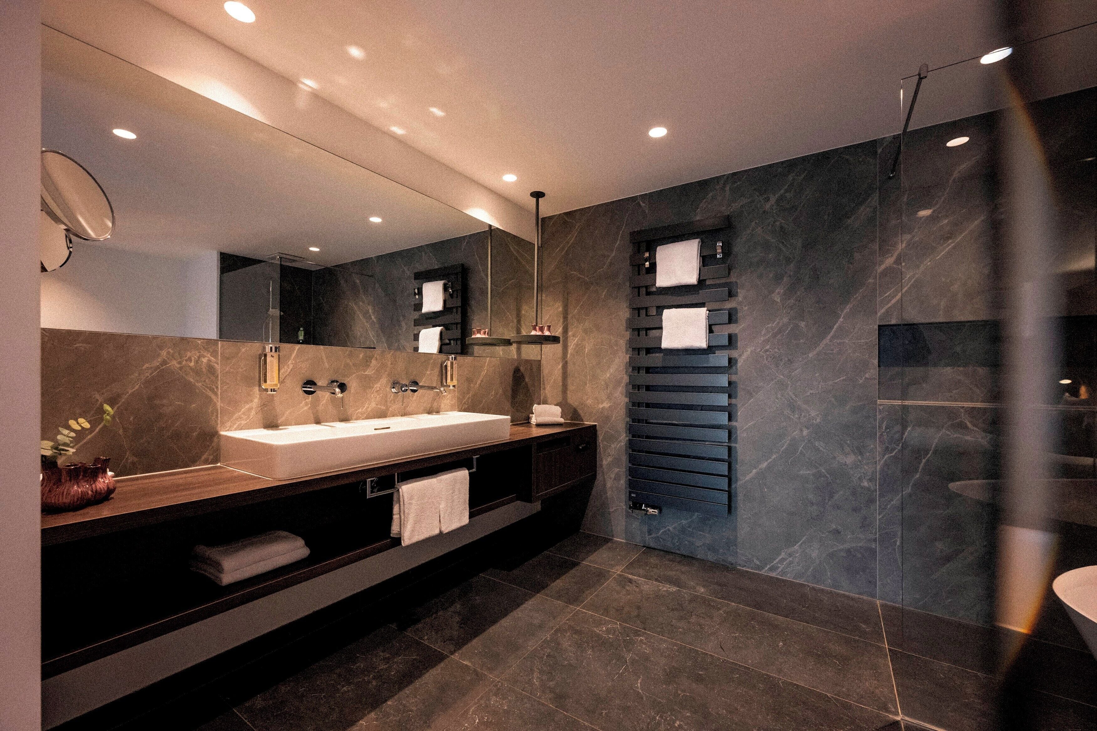A modern bathroom with a large mirror, two sinks, a towel rack, and a glass shower enclosure.