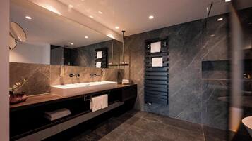A modern bathroom with a large mirror, two sinks, a towel rack, and a glass shower enclosure.