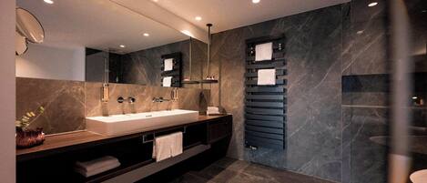 A modern bathroom with a large mirror, two sinks, a towel rack, and a glass shower enclosure.