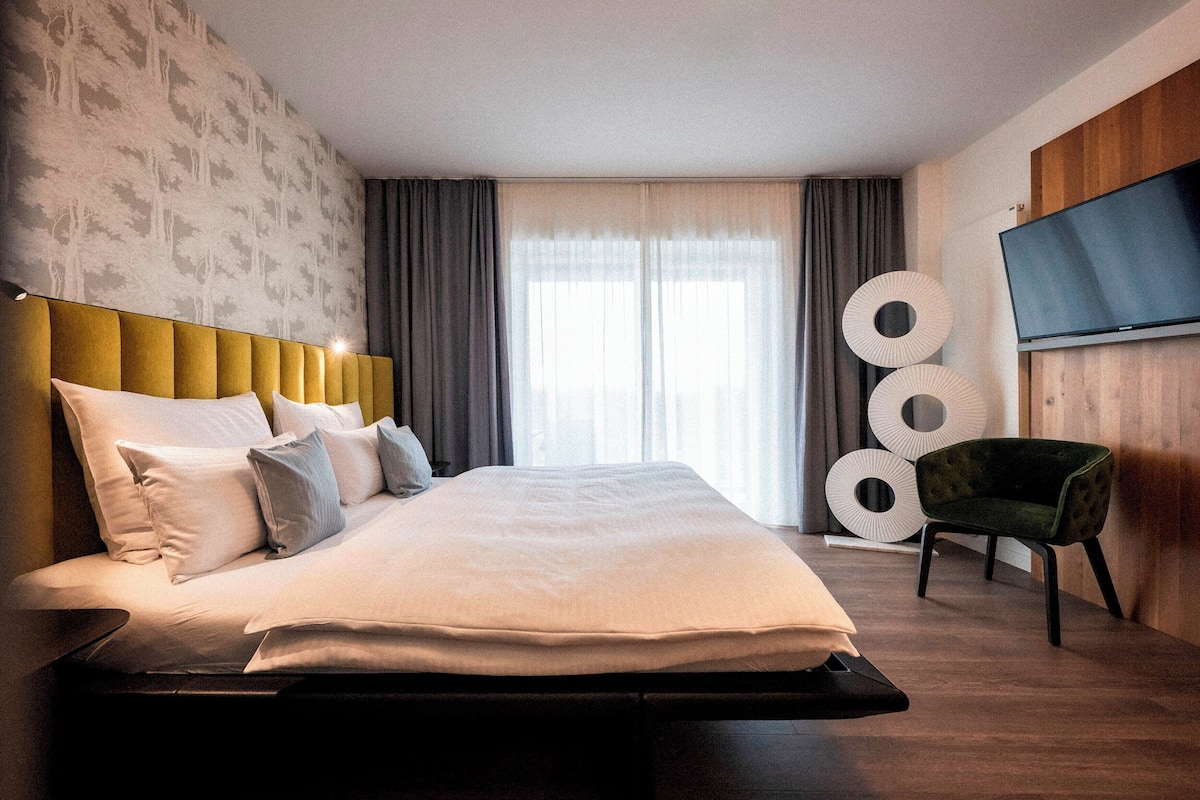 A modern hotel room with a large bed, a flat-screen TV, and a unique wall decor.