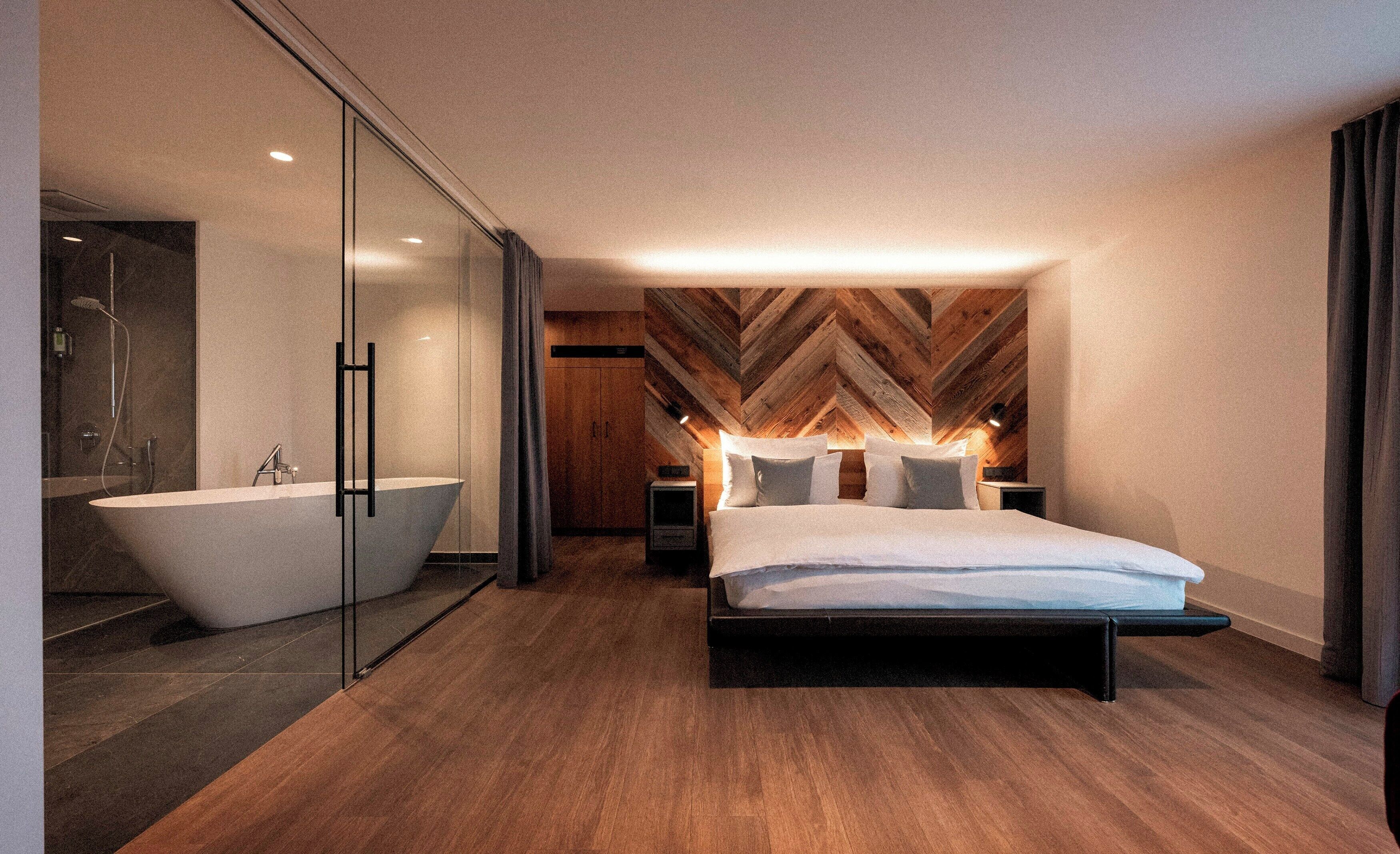 Quarto moderno com cama grande, banheiro separado e banheira livre, além de teto com padrão herringbone.