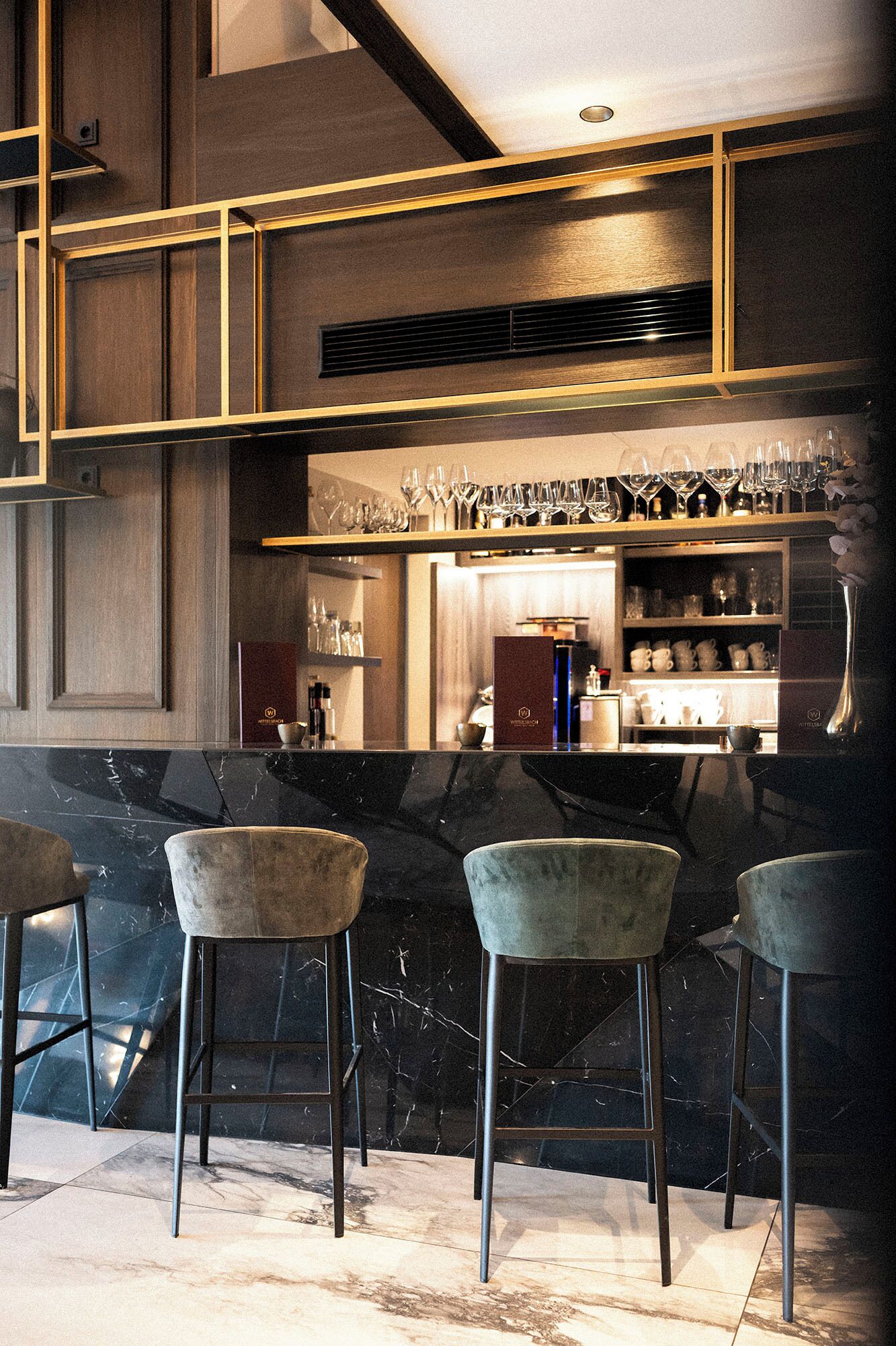 A bar area with three bar stools, a shelf with glasses, and a counter with bottles.