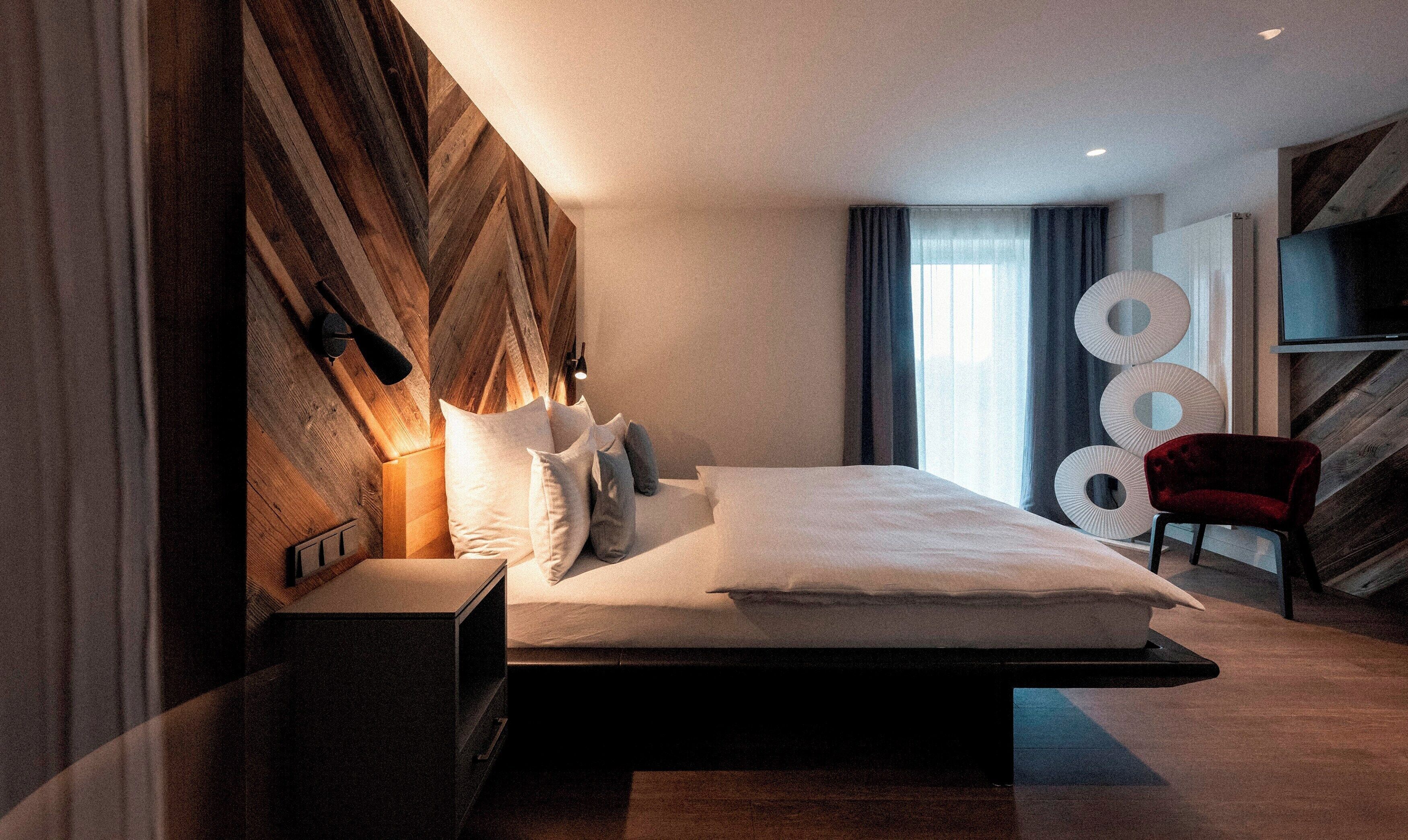 Una habitación de hotel moderna con una cama grande, una mesita de noche, un televisor y una silla roja.