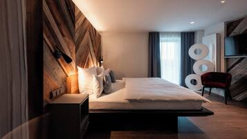 Una habitación de hotel moderna con una cama grande, una mesita de noche, un televisor y una silla roja.