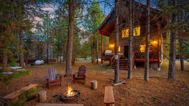 A rustic cabin with a fire pit and seating area surrounded by trees. - The Black Bear Escaped! Hot Tub, Fire Pit , Yellowstone, Golf Course! (Island Park)