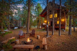 A rustic cabin with a fire pit and seating area surrounded by trees.