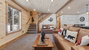 A spacious living area with a wooden interior, a staircase, a leather sofa, and a dining area. - The Black Bear Escaped! Hot Tub, Fire Pit , Yellowstone, Golf Course! (Island Park)
