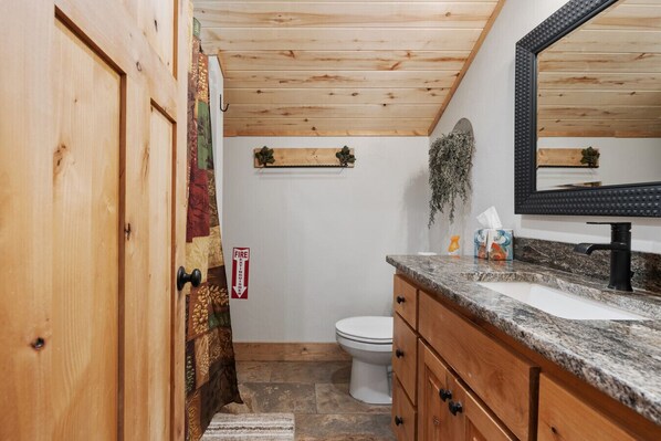 A bathroom with a wooden door, a white toilet, a granite countertop, and a mirror.